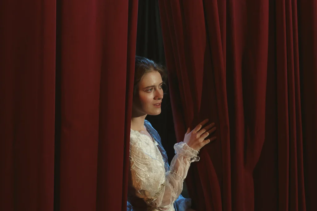 A woman on a theatre stage having a look from the red curtain