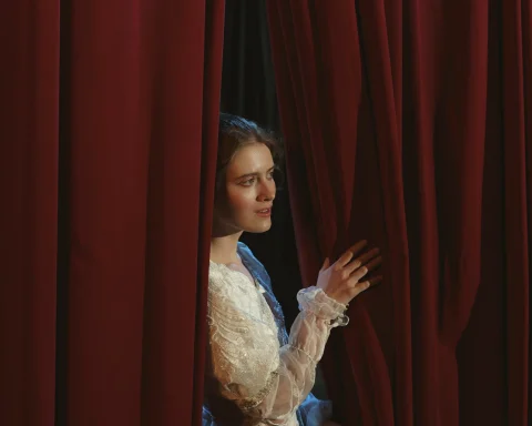 A woman on a theatre stage having a look from the red curtain