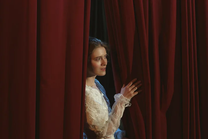 A woman on a theatre stage having a look from the red curtain