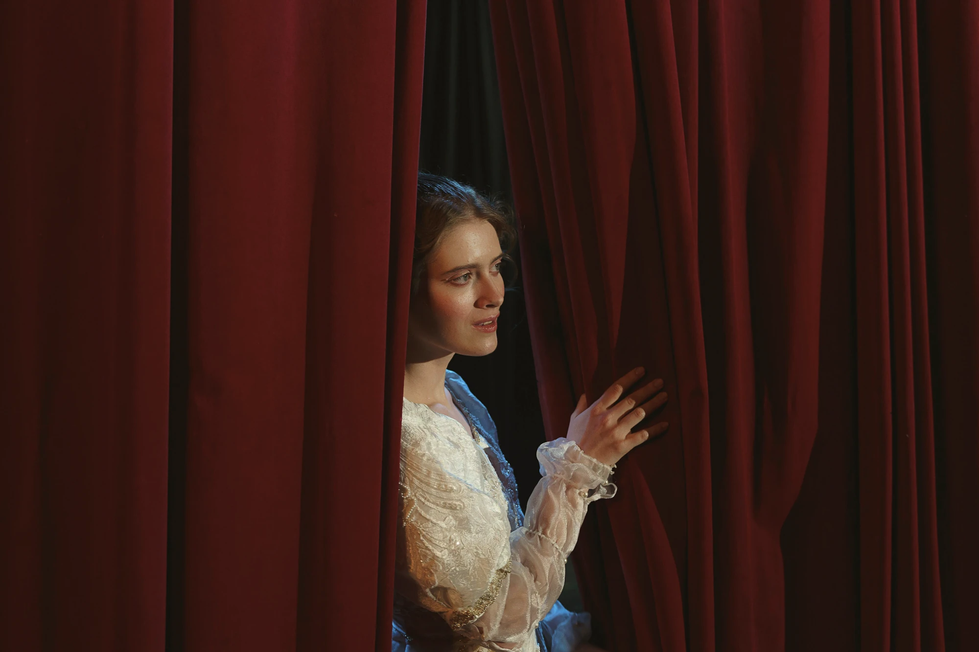 A woman on a theatre stage having a look from the red curtain