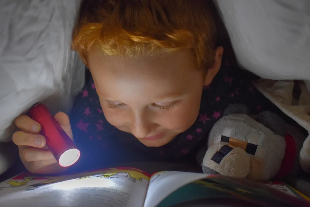 Child reading under the cover with a flashlight