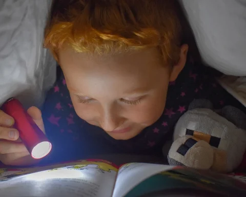 Child reading under the cover with a flashlight