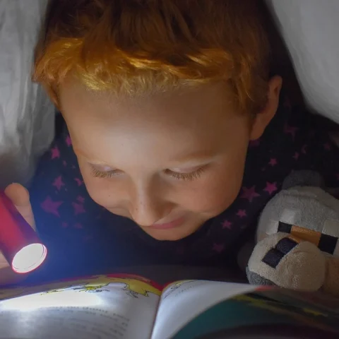 Child reading under the cover with a flashlight