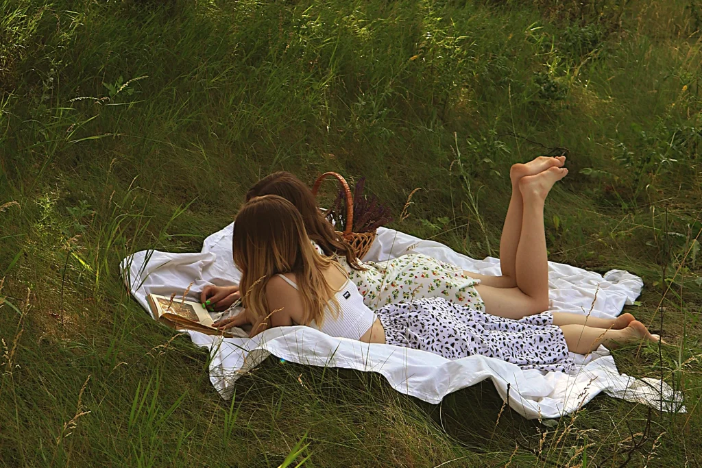 Two girls reading a summer book in a meadow, illustration for 10 classic books to read this summer