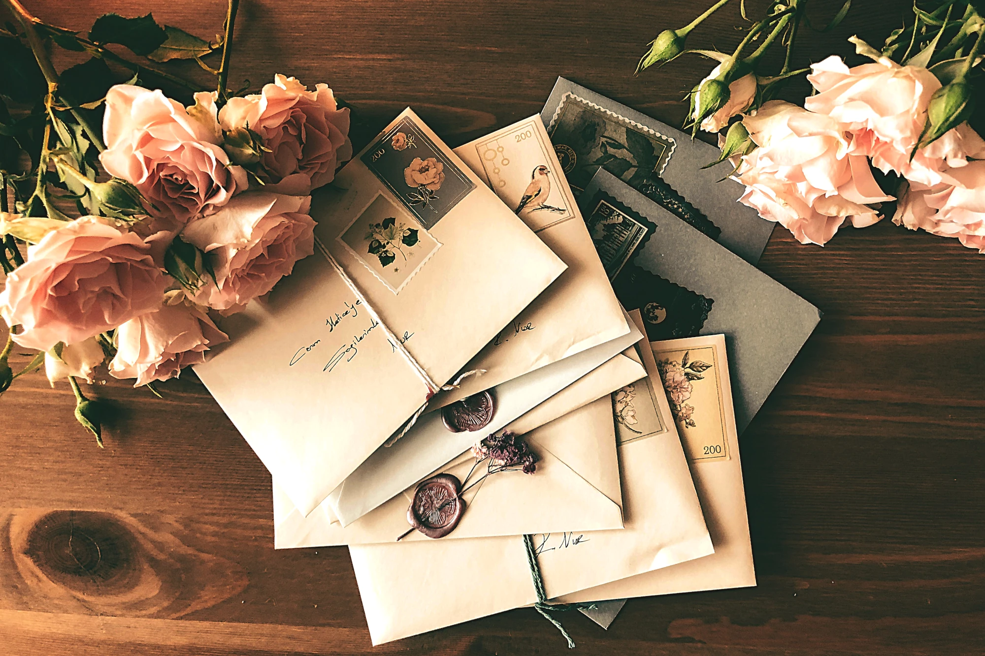 A stack of letters on a wooden table, there are also flowers